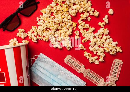 Top view of popcorn, medical mask with cinema tickets and sunglasses on red background Stock Photo