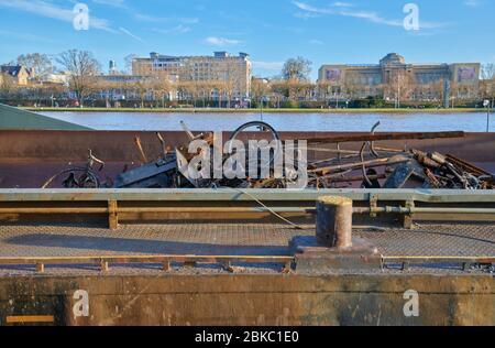 Iron scraps on a boat, on the river Rhine, with Frankfurt museum riverside view in the background