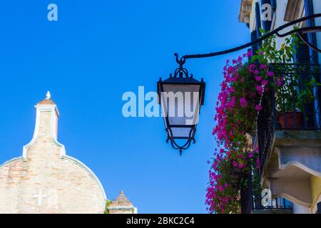 Street vintage lantern,old building with colorful flowers pots at the balcony and church facade in the distance Venice,Veneto,Italy Stock Photo