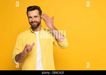 Smiling man looking at camera while using deaf and dumb language on yellow background Stock Photo
