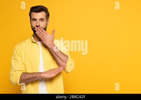 Handsome man covering mouth while using sign language on yellow background Stock Photo