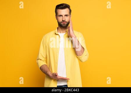 Man looking at camera while using gesture from sign language on yellow background Stock Photo