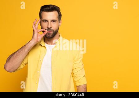 Handsome man using sign language and looking at camera on yellow background Stock Photo