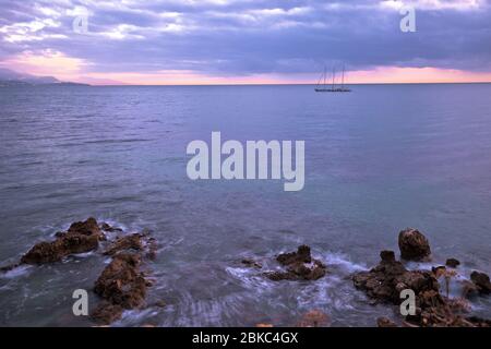 Sailboat on French riviera coast on moody sunset view. Town of Antibes waterfront. France. Stock Photo