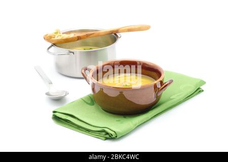 Brown ceramic bowl of hot chicken noodle soup with cooking pot in the background.  Photographed on a white background, Stock Photo
