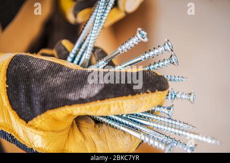 Construction Metal Screws in Worker's Hand. Industrial Theme. Safety Gloves. Stock Photo