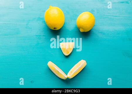 Smiling face made from half of ripe yellow fruit on blue background top view, happy diet, lemons and summer concept. Stock Photo