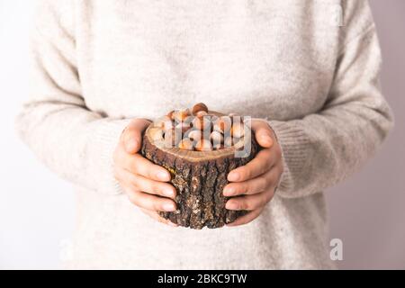 Woman holding shelled hazelnuts in wooden bowl. Natural and unroasted nuts. Organic, healthy and delicious snacks, foods. Stock Photo