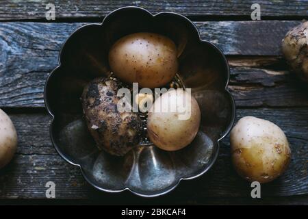 Dirty and washed young raw potatoes in a bowl on a wooden old table Stock Photo