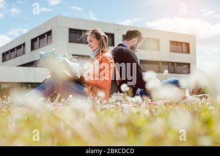 Man and woman student sitting in the grass on university campus Stock Photo