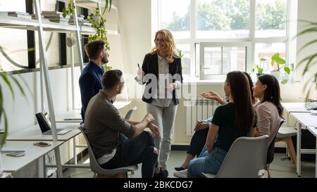 Smiling female leader, coach holding briefing for multiracial team interns. Stock Photo