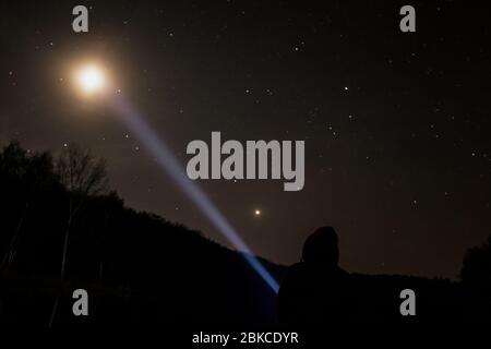 Man standing under the starry sky and shining a flashlight on the moon Stock Photo