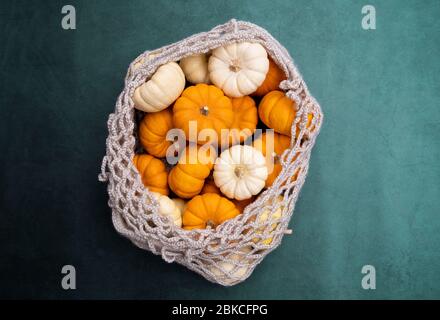 Orange and white pumpkins in mesh shopping bag on dark blue stone background. Top view of freshly harvest organic and natural little pumpkins Stock Photo