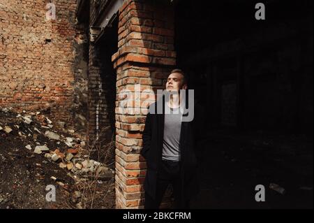 Young man in the coat leaning against the wall in the abandoned buiding Stock Photo