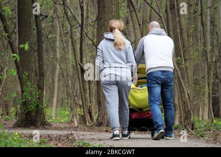 Couple with a baby stroller walking in spring park. Quarantine in a city during covid-19 coronavirus pandemic, concept of motherhood, parents Stock Photo