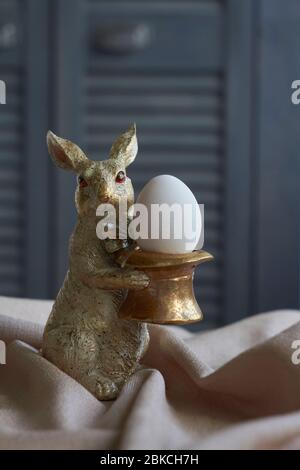 Spring composition, golden rabbit figurine with egg on beige tablecloth, Easter concept, selective focus Stock Photo