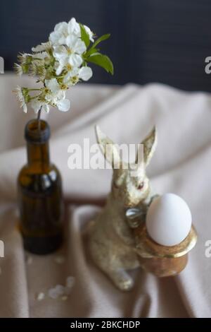 Spring composition, golden rabbit figurine with egg on beige tablecloth and vase with flowering twig, Easter concept, selective focus Stock Photo