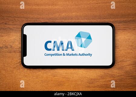 A smartphone showing the CMA (Competition and Markets Authority) logo rests on a plain wooden table (Editorial use only). Stock Photo