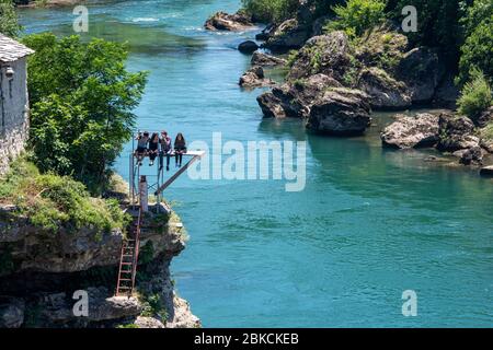 Bosnia and Herzegovina, Mostar - June 2018: Teenagers sit on a diving platform over the river watching drivers leap from the Stari Most bridge Stock Photo