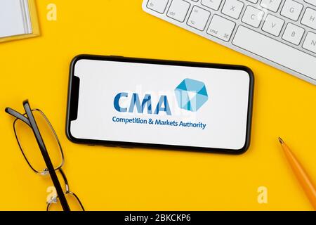 A smartphone showing the CMA (Competition and Markets Authority) logo rests on a yellow background (Editorial use only). Stock Photo