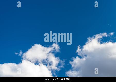 Sunlit blue sky background with copy space and group of white precipitation clouds. Scenic view on dramatic airy cloudscape and flowing puffy cumulus. Stock Photo