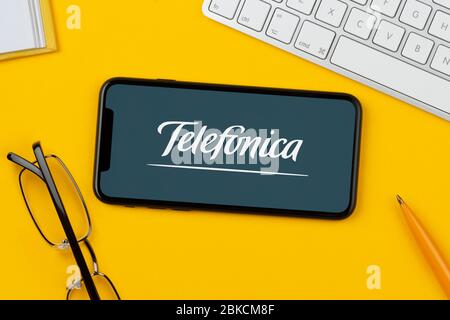 A smartphone showing the Telefonica logo rests on a yellow background along with a keyboard, glasses, pen and book (Editorial use only). Stock Photo