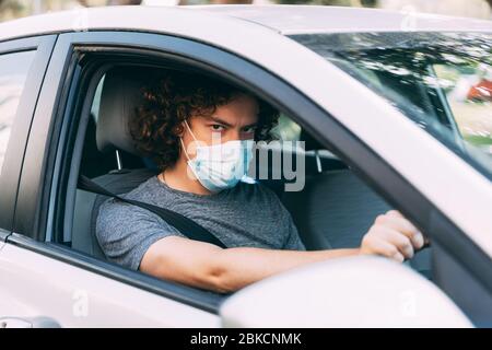 A man drives a car in a medical mask. A man in a protective mask sits behind the wheel of a car. Taxi driver in mask. Protection from coronavirus epid Stock Photo