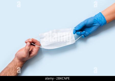 Men's and women's hands in latex gloves holding one medical mask. Stock Photo