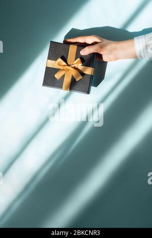 Vertical photo with gift box in a female hand on sunlights on blue background. Flat lay, top view, place for text. Stock Photo