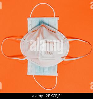 Medical mask with valve and surgical mask on orange background 2021. Conceptual photo with cross-shaped masks as a symbol of protection against diseas Stock Photo
