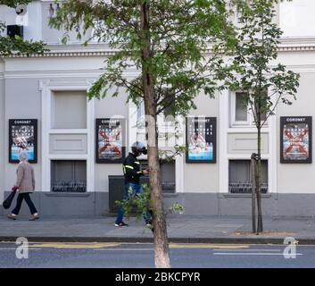 Two people walk by The Coronet theatre, displaying posters for productions Another Look at Memory and Youth Without God, Notting Hill, West London. Stock Photo