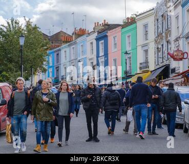 People walking in the street at Portobello Market, with colourful terraces in background. Portobello Road, Notting Hill, West London, England, UK Stock Photo