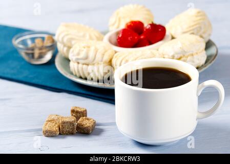 White Cup of americano coffee, and white marshmallow or Zephyr , on a light blue wooden background. Stock Photo