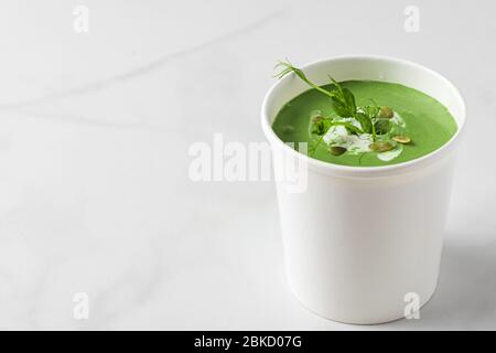 Green cream soup in paper package or disposable cup with pea and spirulina. Vegan food delivery concept. mock up Stock Photo