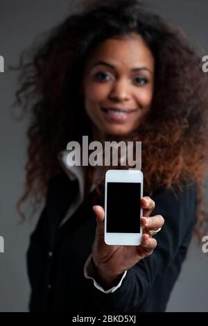 Smiling friendly woman holding out a mobile phone extended to the camera with a blank screen and focus to the cellphone Stock Photo