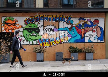 Portland, USA. 03rd May, 2020. A man walks his dog past street art by artists VMO and Anna Deez Nutz praising essential workers as heroes on a boarded up business in Portland, Ore., on May 3, 2020. (Photo by Alex Milan Tracy/Sipa USA) Credit: Sipa USA/Alamy Live News Stock Photo