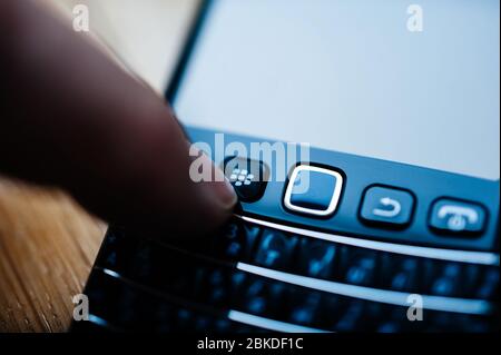 London, United Kingdom - April 21, 2013: Blue color cast man hand pressing the Blackberry home button on the vintage smartphone telephone with full qwerty keyboard Stock Photo