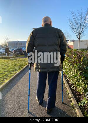 Strasbourg, France - Jan 20, 2020: Vertical image rear view of senior man walking with canes in large French hospital parking Stock Photo