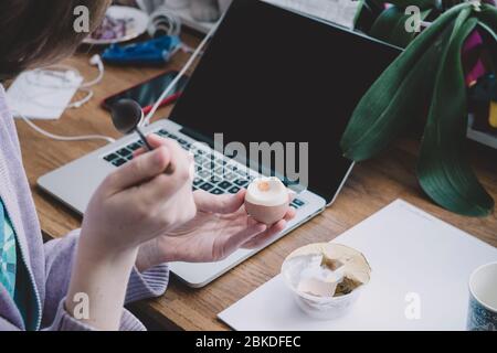 Side view of a lonely woman working from home eating a boiled egg during her teleworking session - worldwide epidemy of Coronavirus COVID19 has put people in lockdown and tele working Stock Photo