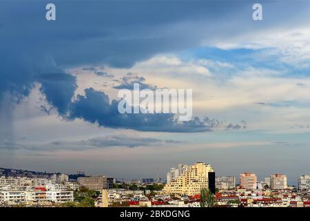 Dark rain stormy clouds approach the city and cover the blue sky and sunlight. The season of spring thunderstorms has begun. Scenic cityscape. Stock Photo