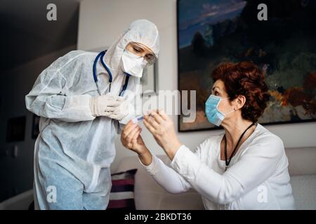 Coronavirus frontline doctor home treatment of senior COVID-19 patient.Home visit for treating infectious disease.Healthcare worker in PPE hazmat suit Stock Photo