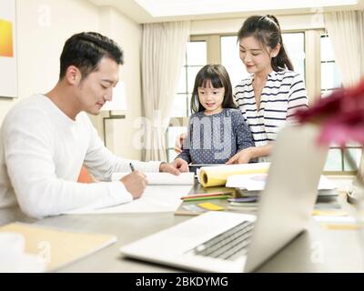 young asian mother and daughter watching father drawing a design while working from home (artwork in background digitally altered) Stock Photo