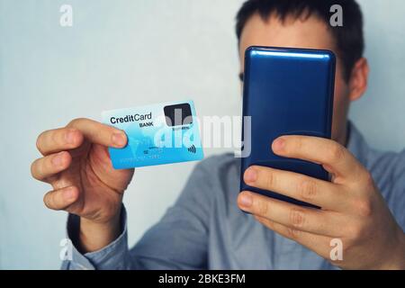 Cropped shot of male in shirt making online payment via plastic card and smart phone. Unrecognizable man holding mobile and credit card with biometric Stock Photo