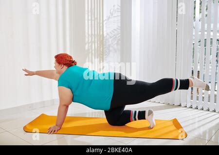 Young plus size woman doing table top exercise on yoga mat at mat to stabilize her core Stock Photo