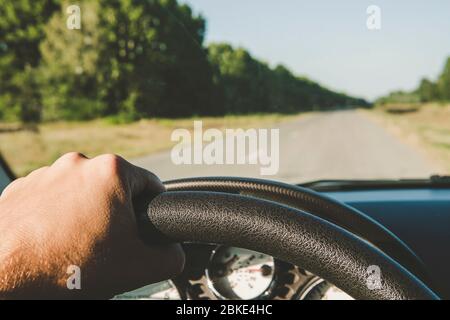 Hands of a driver on steering wheel of a car and empty asphalt road. Riding behind the wheel of a car in summer. first-person view. drive on the highw Stock Photo