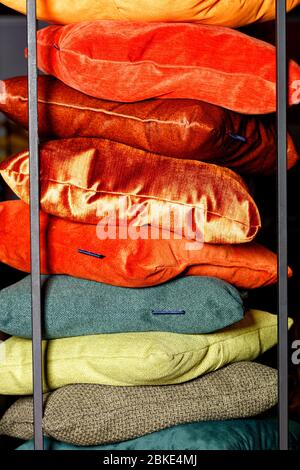 Collection Red, orange, yellow, green, terracotta shades of textile stacks of decorative pillows on a dark background with a metal frame. Stock Photo
