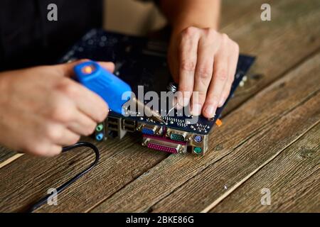 Technician or engineer is focused on repairing electronic circuit board with soldering iron. Man hands soldiers computer circuit board using soldering Stock Photo
