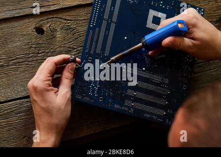 Technician or engineer is focused on repairing electronic circuit board with soldering iron. Man hands soldiers computer circuit board using soldering Stock Photo