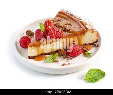 piece of caramel cheesecake decorated with fresh raspberries and mint leaves on white plate Stock Photo