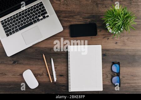 Flatlay with opened notepad, laptop, smartphone, glasses and plant on wooden table of freelancer Stock Photo